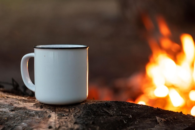 Camping en el bosque Taza de camping blanca con té sobre un fondo de fuego Camping de verano Relajación en la naturaleza