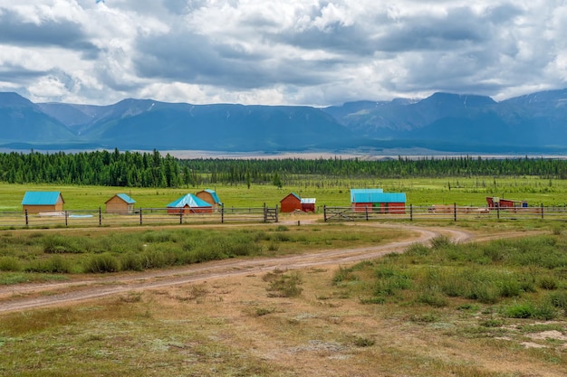 Camping colectivo a las casas de huéspedes de madera del complejo turístico de distancia contra el fondo de verdes colinas Granja en la estepa Campo en las tierras altas Pueblo de Kurai Siberia Altai