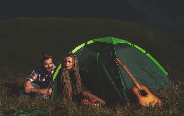 Camping feliz hombre y mujer sonriendo y tocando canciones en la guitarra mientras acampa en las montañas