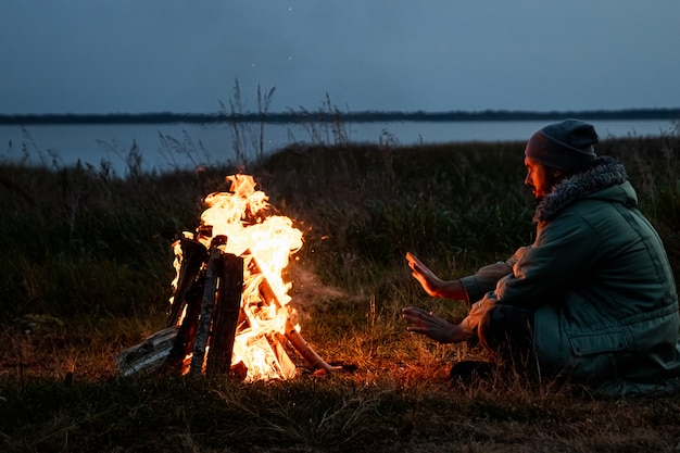 Camping homem sentado perto do fogo à noite contra o céu. viagens, turismo, camping.