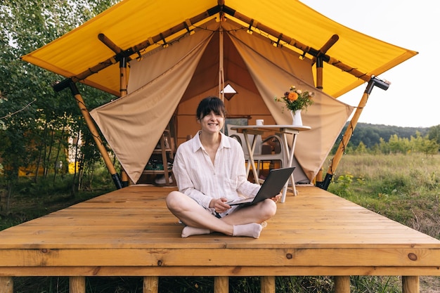 Camping mujer joven sentada en una tienda de campaña amarilla Chica feliz relajándose y trabajando en vacaciones