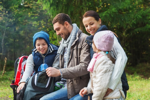 Camping-, Reise-, Tourismus-, Wander- und People-Konzept - glückliche Familie mit Rucksäcken und Thermoskanne im Camp