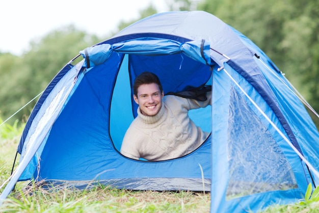 Camping-, Reise-, Tourismus-, Wander- und Personenkonzept - lächelnder männlicher Tourist im Zelt