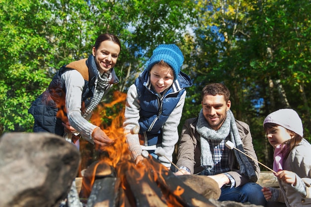 Camping-, Reise-, Tourismus-, Wanderungs- und Personenkonzept - glückliche Familie, die Marshmallow über dem Lagerfeuer röstet