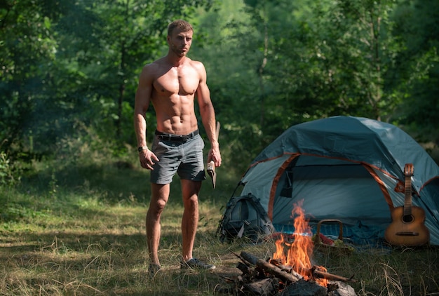 Camping Saison mit Lagerfeuer Mann mit nacktem Oberkörper Picknick Tourismus Camp Mann Holzfäller mit Axt Blick a