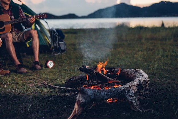 Camping tienda de campaña en la naturaleza amigos felices grupo noche fiesta hoguera y tocar guitarra juntos en verano en el bosque natural