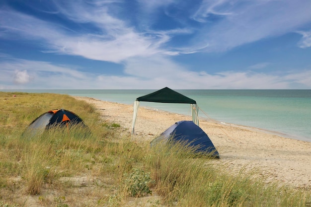 Camping- und Touristenzelt an einer wilden Küste am Meer, früh morgens vor blauem Himmel mit Wolken. Foto in hoher Qualität