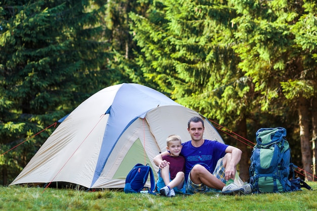 Camping de vacaciones el padre le muestra a su hijo algo a distancia descansando cerca de la tienda después de caminar en el bosque. viajar y actividades al aire libre. relaciones familiares felices y estilo de vida saludable.