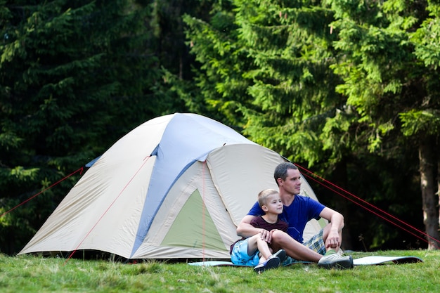 Camping de vacaciones Padre y su hijo descansando cerca de la tienda después de caminar en el bosque. Viajes y actividades al aire libre. Relaciones familiares felices y estilo de vida saludable.