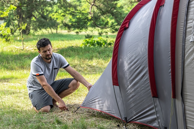 Camping, viajes, turismo, concepto de caminata - joven montando carpa en el bosque.