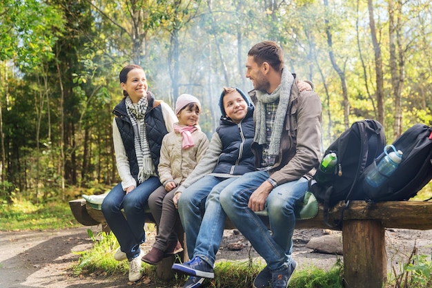 camping, viajes, turismo, senderismo y concepto de personas - familia feliz sentada en un banco y hablando en el campamento en el bosque