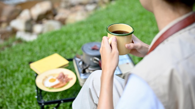 Campista asiática relaxada cortada tomando café da manhã enquanto acampa no acampamento