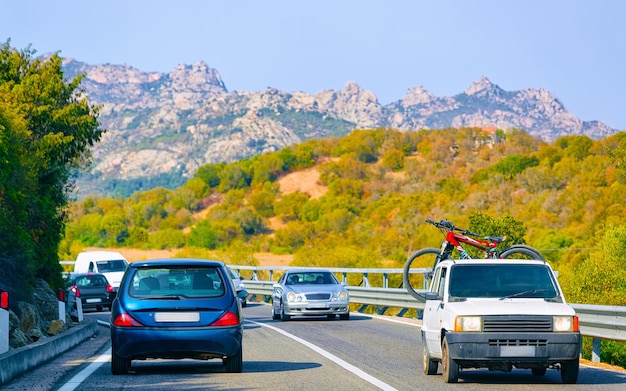 Campista com bicicletas na estrada na Costa Esmeralda no mar Mediterrâneo na ilha da Sardenha, Itália verão. Autocaravana de caravana de férias na estrada. Minivan rv na auto-estrada. Mídia mista.