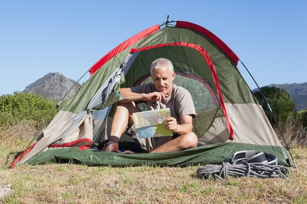 Campista feliz olhando o mapa sentado na sua tenda