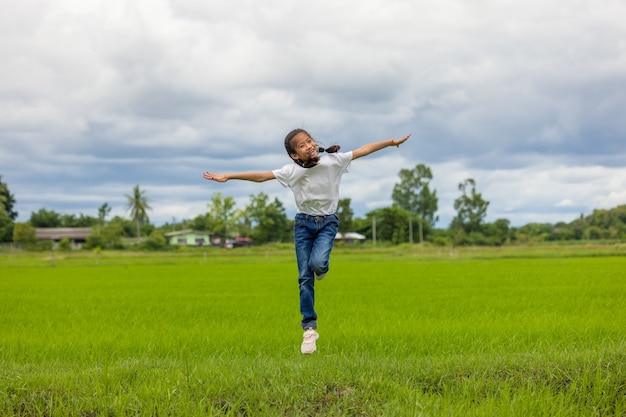 En un campo de arroz de cultivo orgánico, los niños asiáticos felices saltando levantan sus manos hacia el cielo y sonríen.