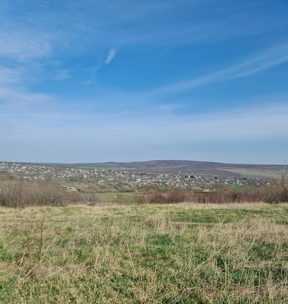 Un campo con una colina al fondo y un campo grande con un pequeño pueblo a lo lejos.