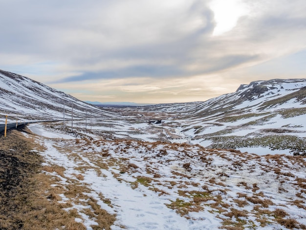 Campo com neve no inverno com montanhas ao fundo sob céu azul nublado na Islândia