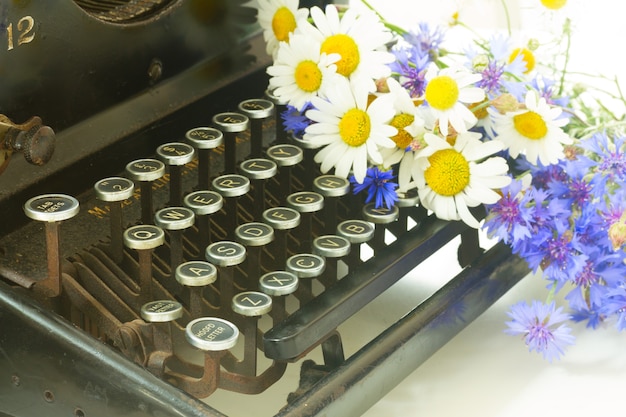 Campo dasies frescas y flores de maíz y máquina de escribir vintage negra de cerca