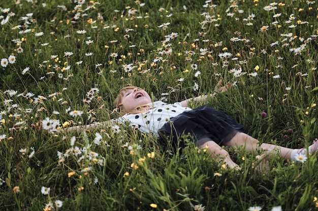 Campo de camomila e criança ao pôr do sol Menina de vestido encontra-se no campo de camomila e sorri