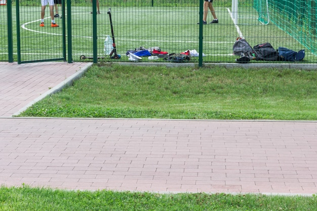 Campo de esportes para a prática de futebol. mochilas dos jogadores perto da cerca, pés dos jogadores de futebol no campo. copie o espaço