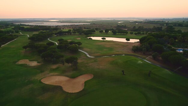 Foto campo de golfe vista superior dos greens, lagos de estrada e bunkers de areia no campo de golfe ao pôr do sol