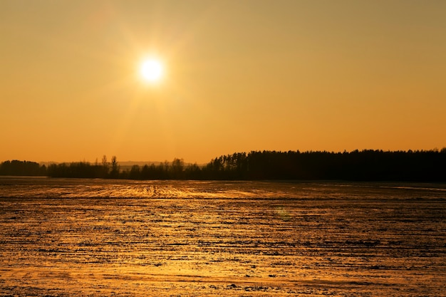 Campo fotografiado cubierto de nieve en la temporada de invierno. La imagen muestra el sol amarillo durante el atardecer.