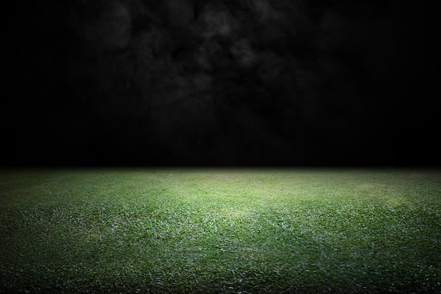 El campo de fútbol vacío de hierba está iluminado por un reflector en un fondo oscuro El campo está listo para un juego
