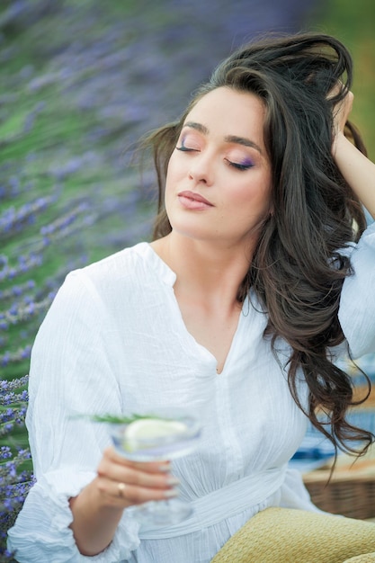 Campo de lavanda Hermosa mujer rizada de pelo oscuro con un vestido blanco sencillo en un campo de flores moradas