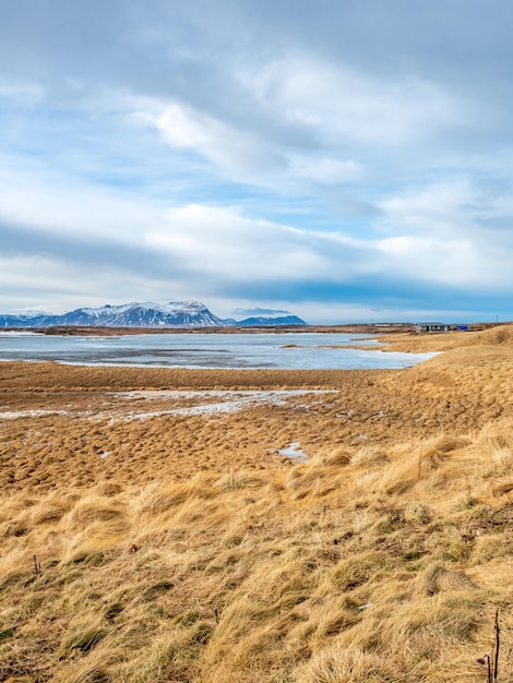 Campo con nieve en invierno con montañas de fondo bajo un cielo azul nublado en Islandia