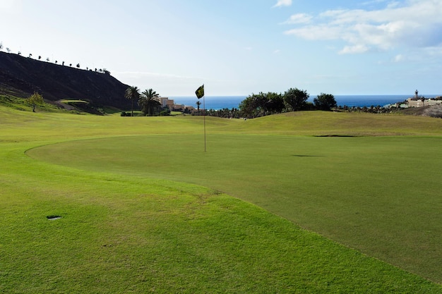 campo verde para practicar golf con bandera y playa al fondo