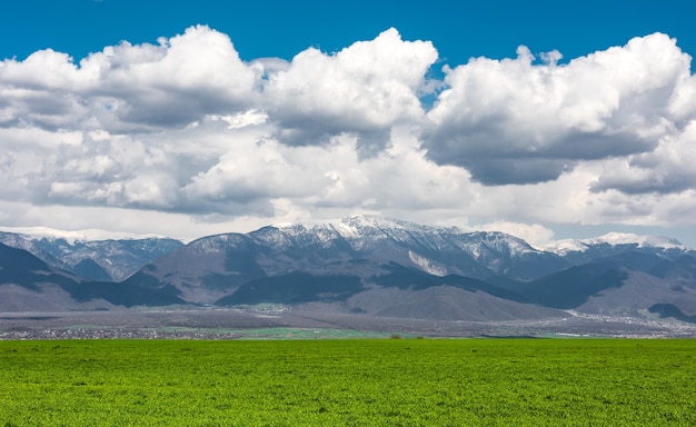 Campos verdes de fazenda perto de montanhas com nuvens