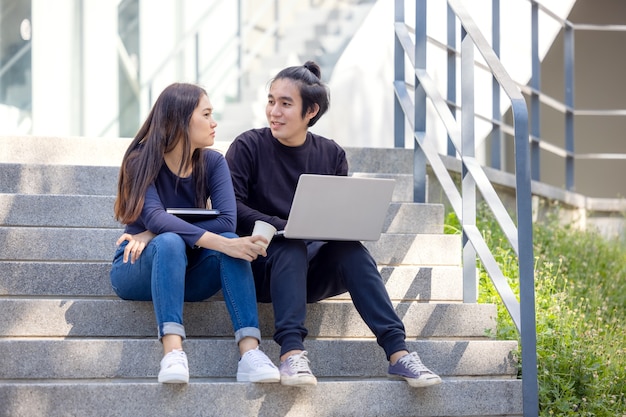 En el campus universitario, dos parejas asiáticas se sientan en la escalera con el pulgar hacia arriba, trabajando en computadoras portátiles.