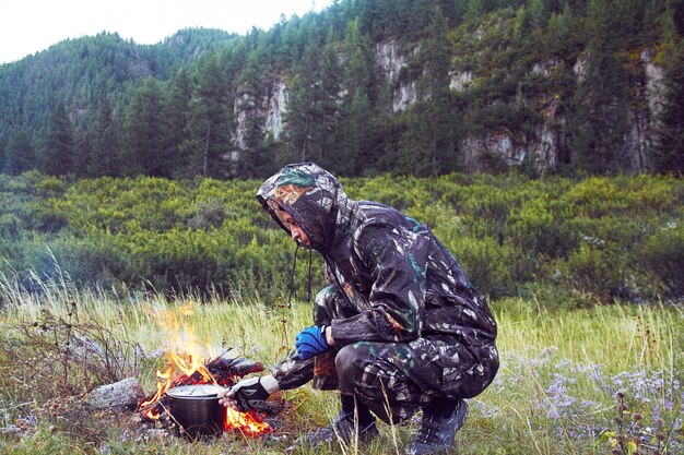 Camuflagem de homem preparando comida na fogueira sobreviver