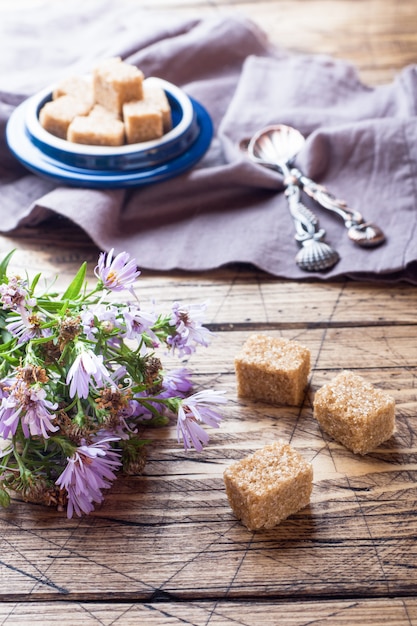 Caña de azúcar de Brown y un ramo de flores en una tabla de madera.