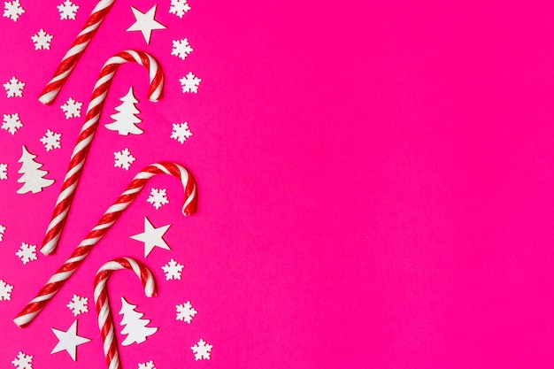 La caña de caramelo de Navidad estaba colocada uniformemente en fila sobre un fondo rosado con un copo de nieve decorativo y una estrella plana y vista superior