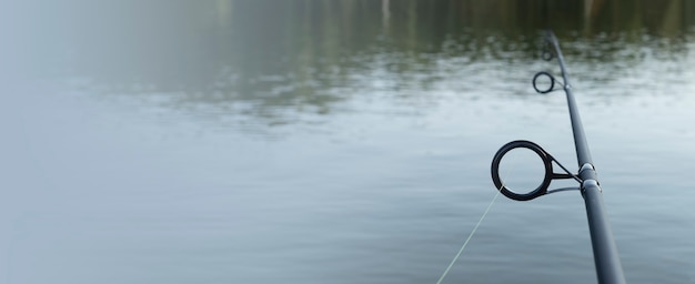 Caña de pescar sobre el agua del lago con espacio de copia para banner de texto