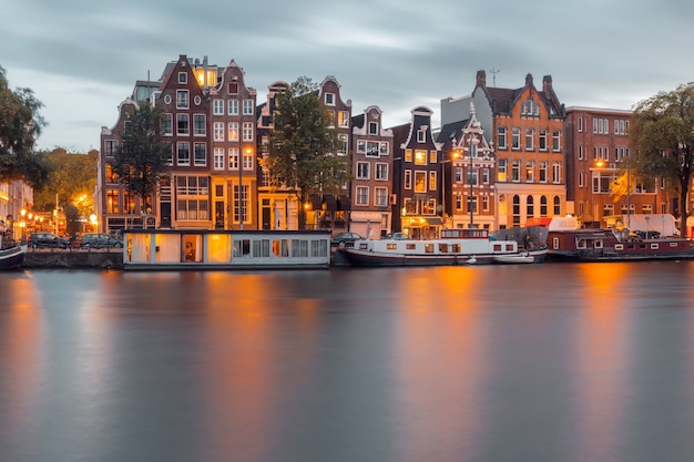 Canal de Amsterdam Amstel con casas y barcos típicos holandeses durante la hora azul crepuscular, Holanda, Países Bajos.