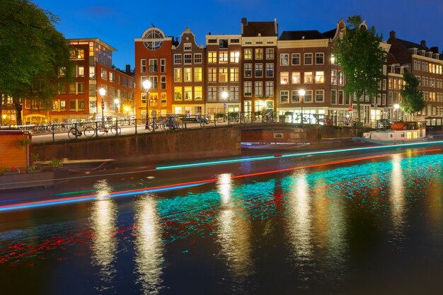 Canal de Amsterdam Prinsengracht con casas típicas holandesas, puente y pista luminosa desde el barco por la noche, Holanda, Países Bajos.