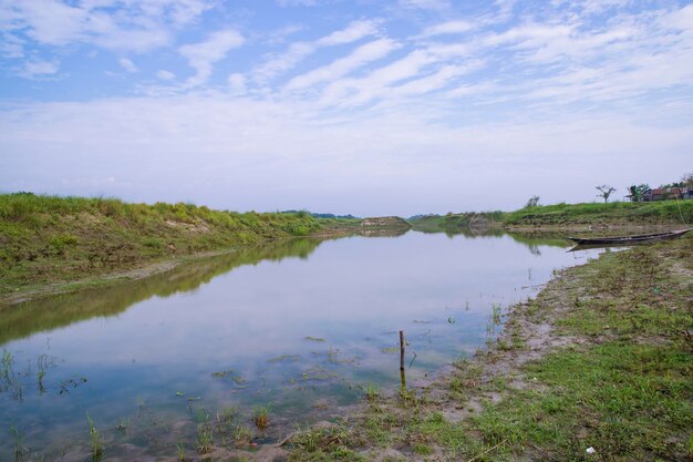 Canal com grama verde e vegetação refletida na água perto do rio Padma em Bangladesh