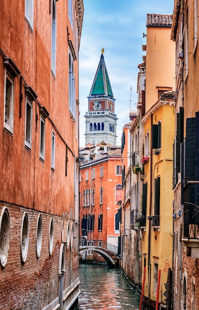 Canal estrecho en Venecia y st. Campanario de Marcus en segundo plano.