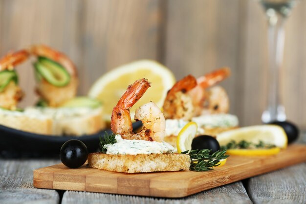 Canapé de aperitivo con camarones y aceitunas en la tabla de cortar en la mesa de cerca