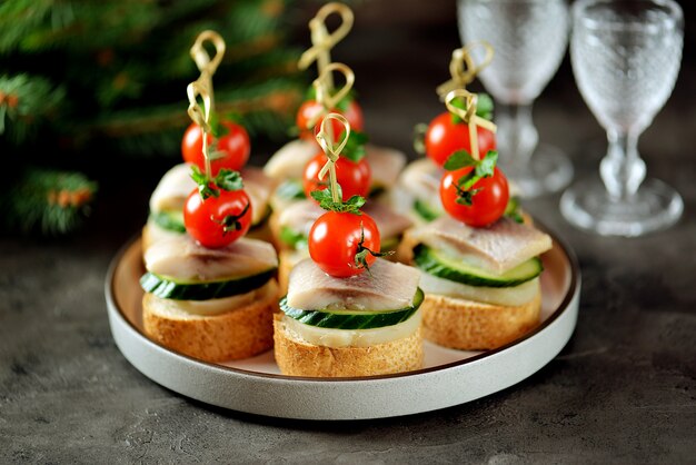 Foto canapé con arenque salado, pepino, patatas hervidas y tomate cherry en crutones