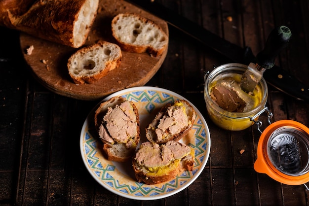 Canape Bruschetta mit Gänseleber Baguette mit gebutterter Gänseleber auf einer Platte auf dunklem Hintergrund