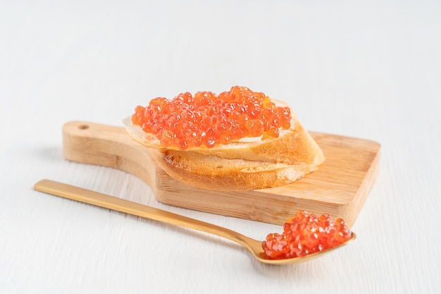 Canape con caviar rojo salado o mantequilla de huevos de pescado y pan con cuchara sobre fondo de madera blanca