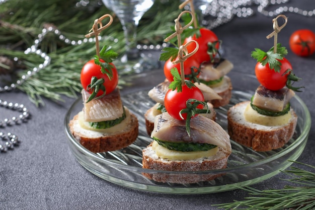 Canapé com batatas cozidas de pepino de arenque salgado e tomate cereja em croutons de centeio em fundo cinza