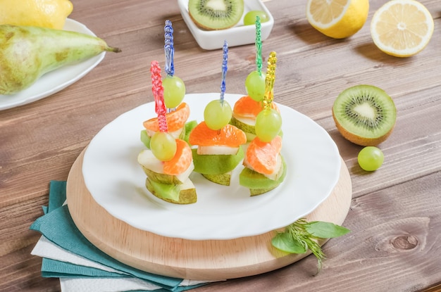 Canape de frutas para una mesa de buffet en un plato de pera kiwi mandarina y uvas sobre un fondo de madera oscura