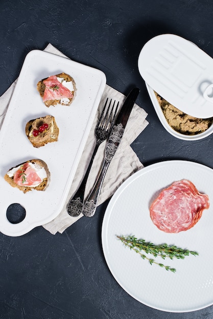 Canapé con jamón, salami y paté de pato en una tabla de cortar blanca y