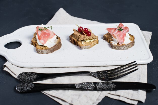 Canapé con jamón, salami y paté de pato en una tabla de cortar blanca y