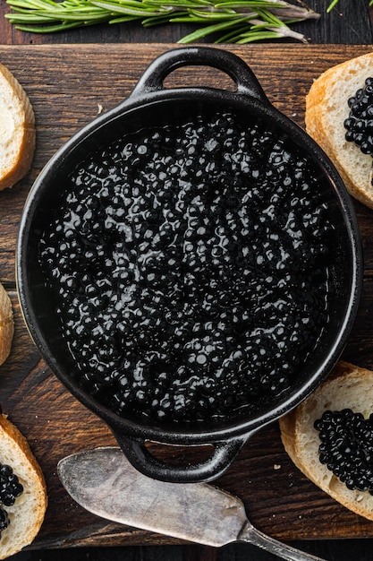 Canapés con caviar de esturión negro, sobre fondo antiguo de mesa de madera oscura, vista superior plana