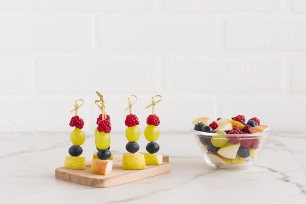 Canapés de frutas suculentas em uma placa de madeira e uma tigela com frutas picadas de banana, pêra, framboesa. comida deliciosa e saudável.